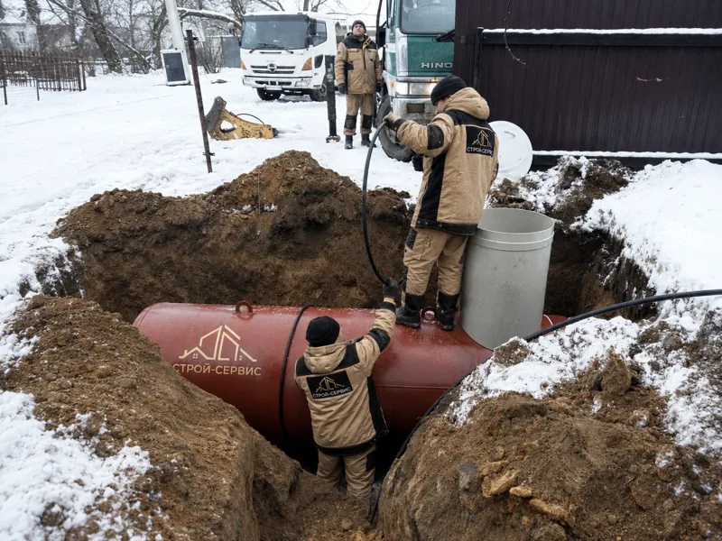 Газгольдер в котловане на заснеженном участке, рядом монтажники